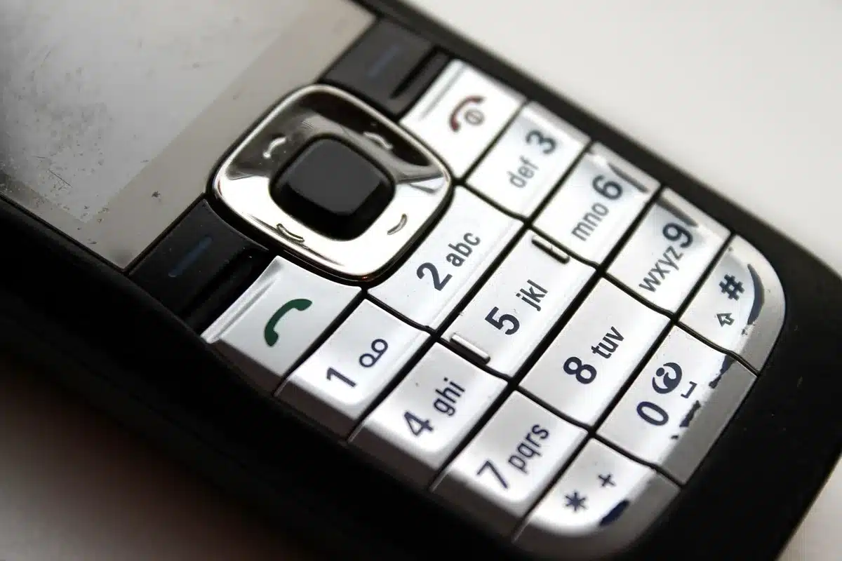 An anonymous hand reaching from bed toward a phone with a key on a table