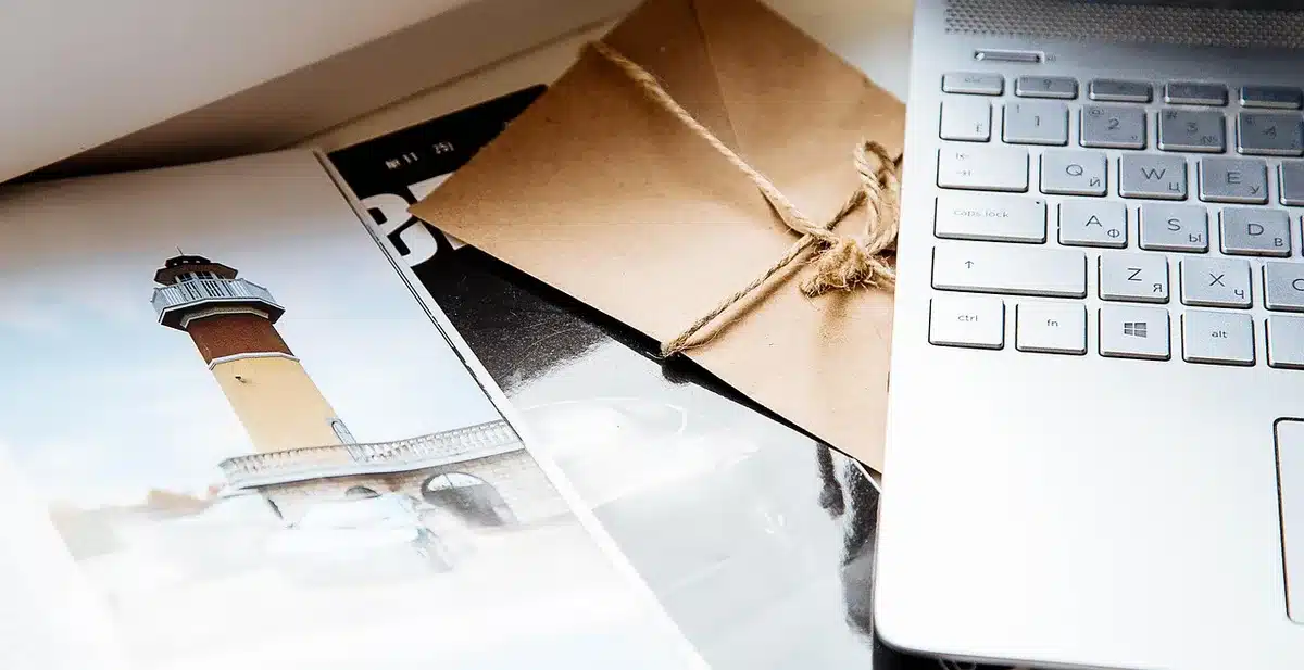 Hands flipping through vintage motorcycle magazines beside a laptop on a workshop bench