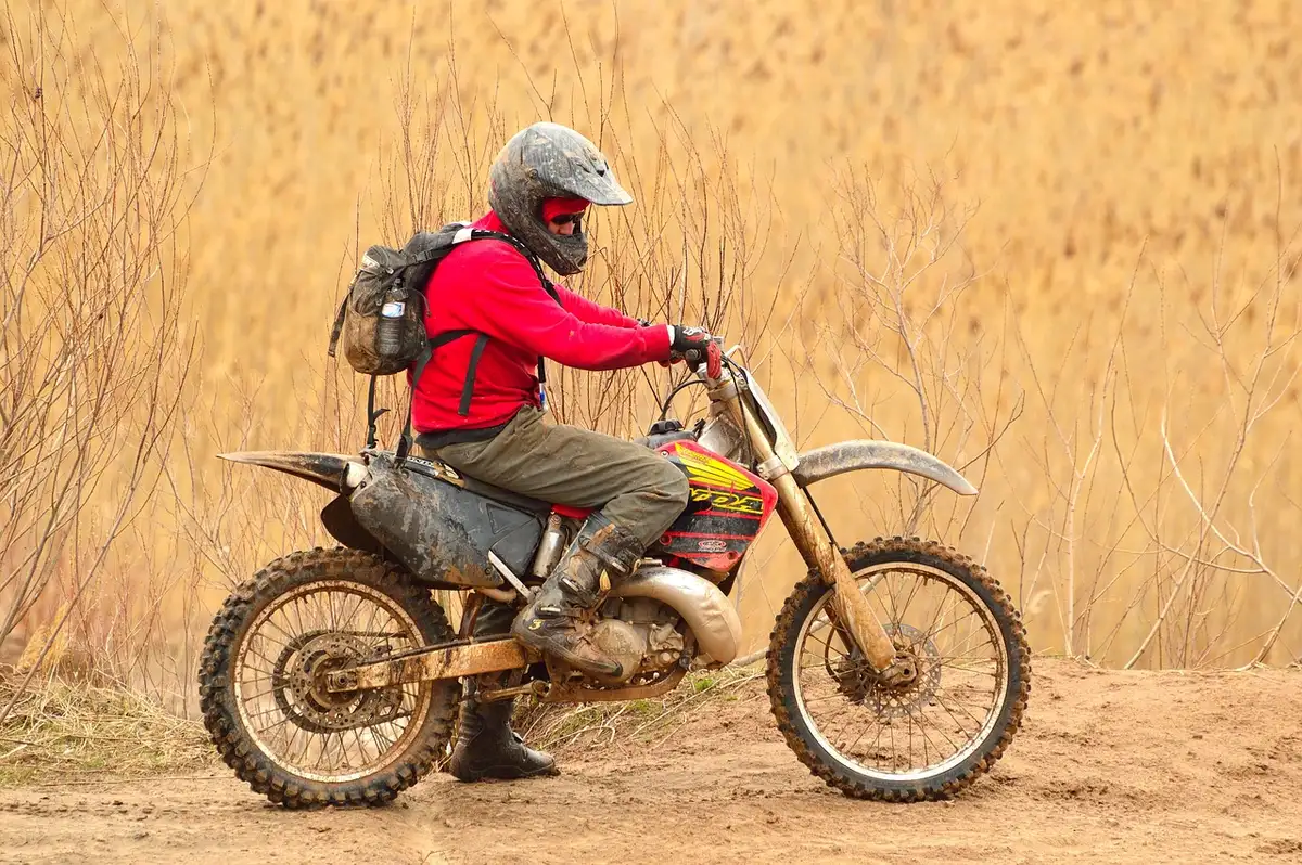 Small off‑road bike riding across a grassy meadow into woodland on a dusty trail