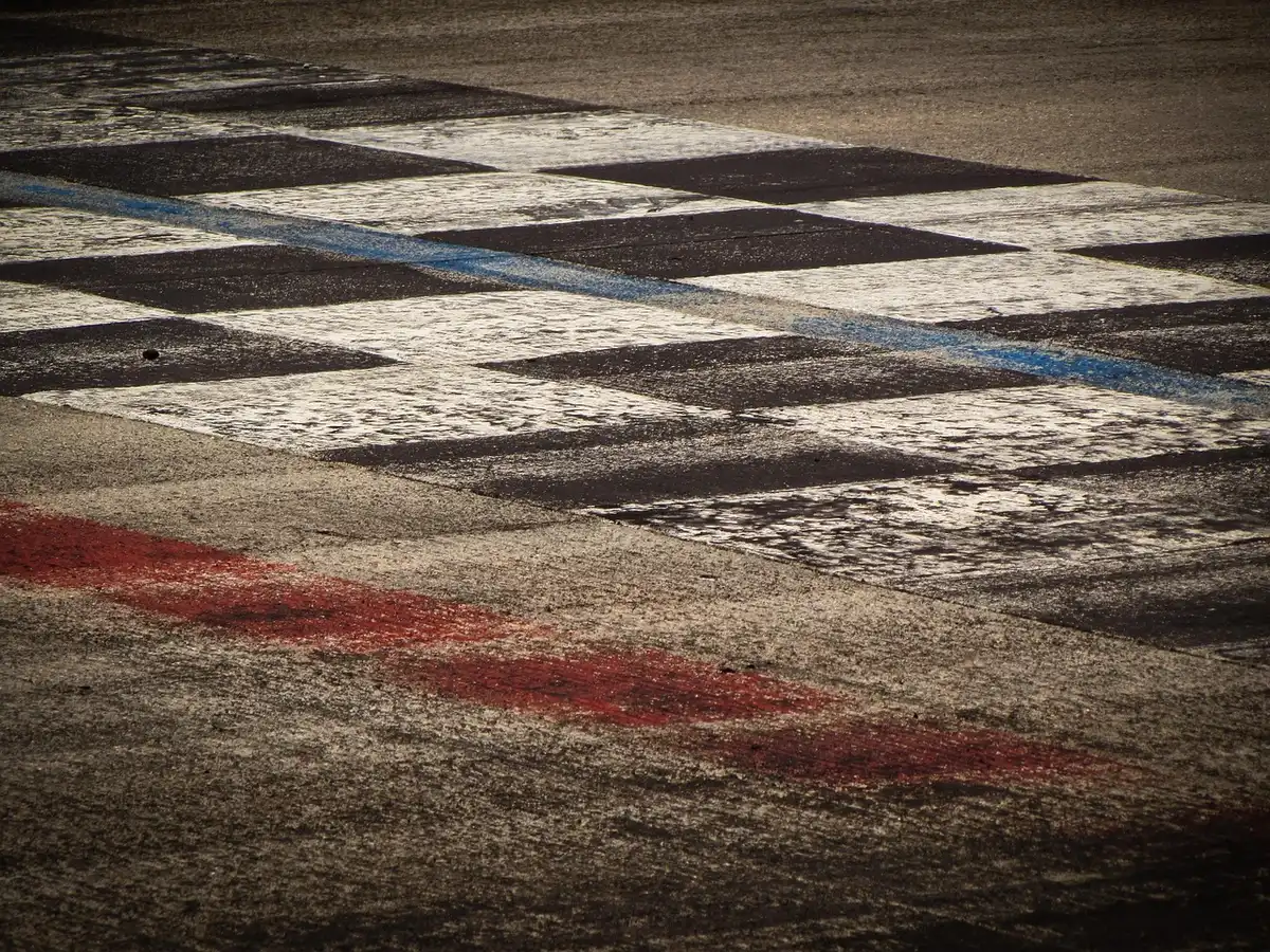 Silhouette of a dragster crossing a dragstrip finish with tire smoke and timing gantry