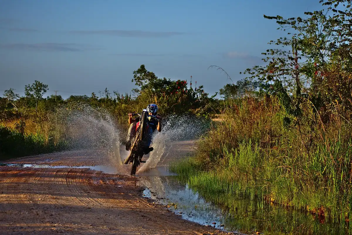 Adventure motorcycle with hard panniers parked on a gravel lane, rider's hands on bars