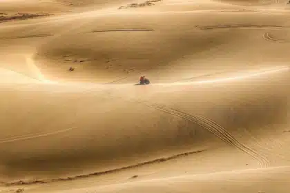 Silhouette of a vintage off-road vehicle and people walking on desert dunes