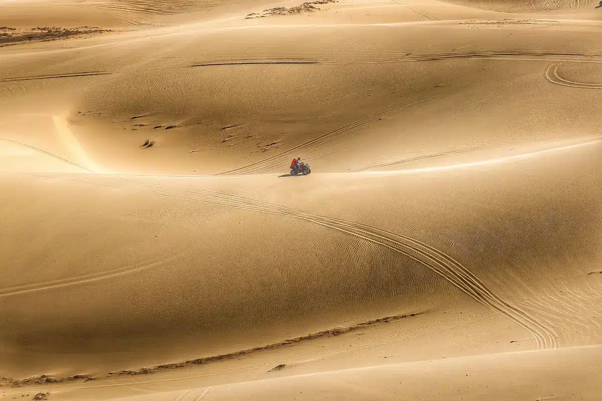 Silhouette of a vintage off-road vehicle and people walking on desert dunes