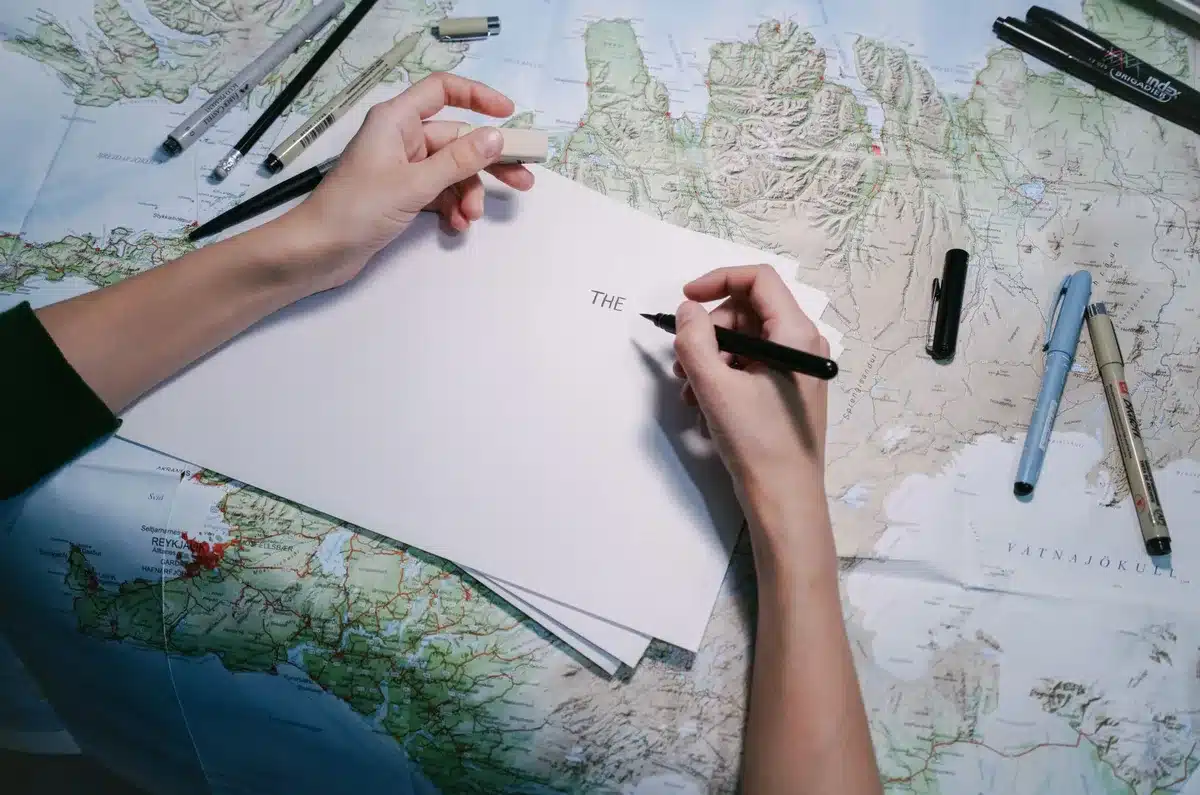 Hands arranging magazine pages and a map on an editor's desk in daylight